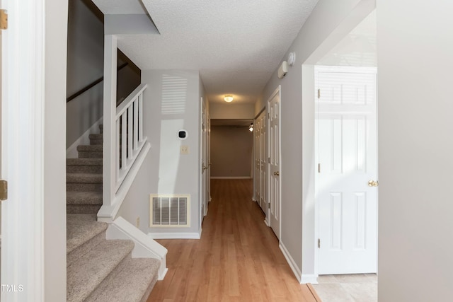 hallway with baseboards, visible vents, light wood-style flooring, stairway, and a textured ceiling