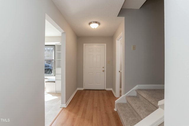 entryway with light wood-type flooring, stairs, baseboards, and a textured ceiling