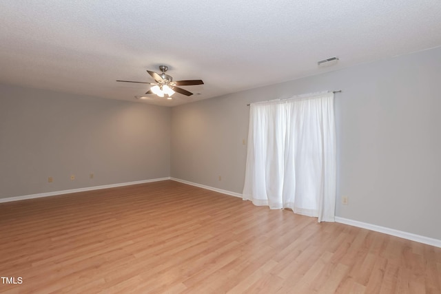 spare room with a textured ceiling, light wood-type flooring, visible vents, and baseboards