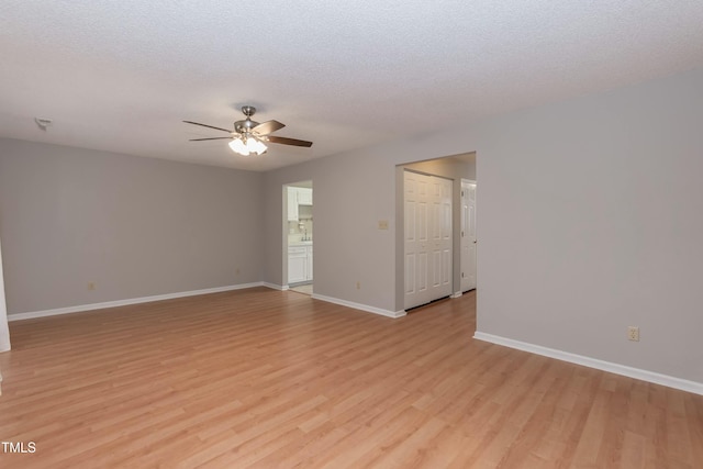 spare room featuring light wood finished floors, baseboards, a ceiling fan, and a textured ceiling