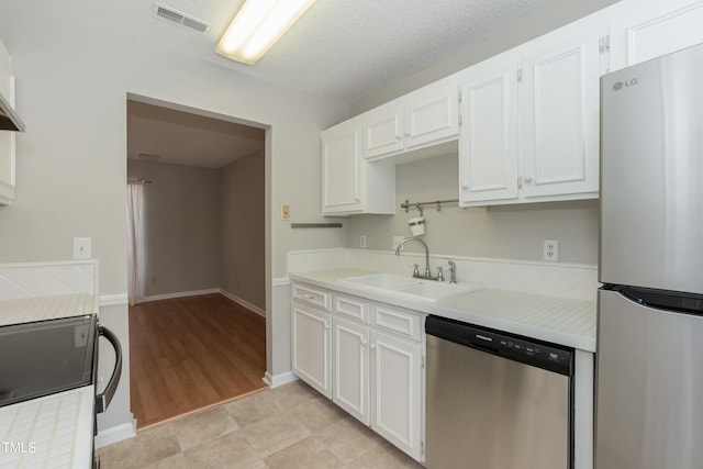 kitchen featuring appliances with stainless steel finishes, white cabinets, light countertops, and visible vents