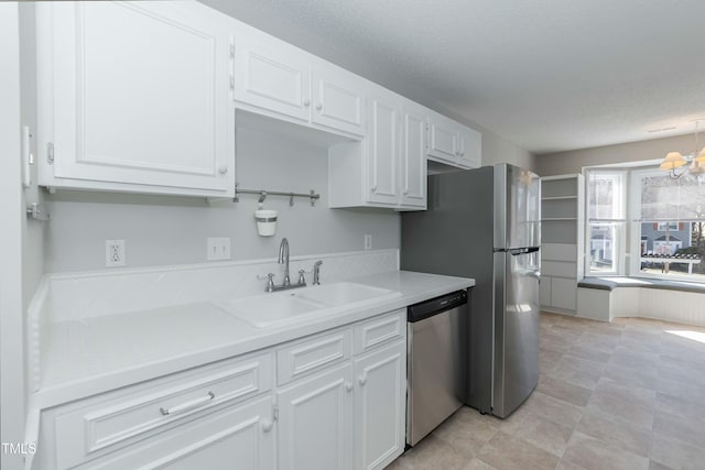 kitchen with appliances with stainless steel finishes, light countertops, a textured ceiling, white cabinetry, and a sink