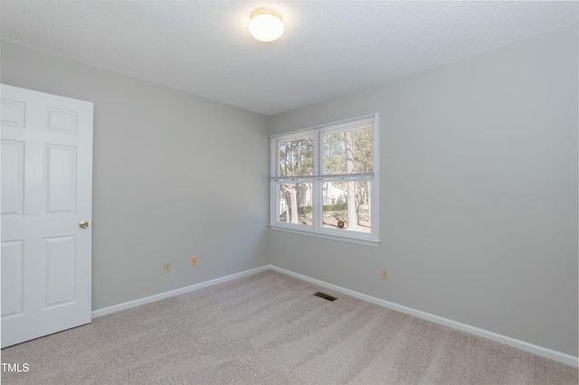 spare room featuring light carpet, a textured ceiling, visible vents, and baseboards