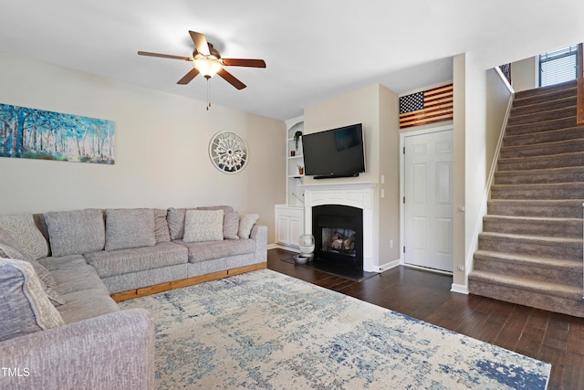 living area with baseboards, wood-type flooring, ceiling fan, stairway, and a fireplace