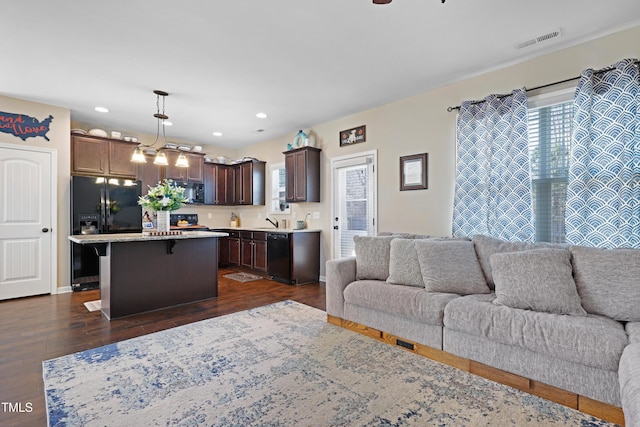 kitchen featuring visible vents, open floor plan, black appliances, dark brown cabinets, and a kitchen breakfast bar