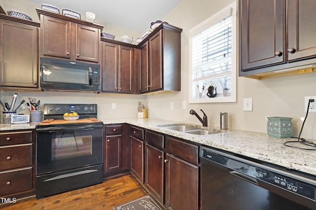 kitchen with light stone counters, dark brown cabinetry, dark wood-type flooring, a sink, and black appliances