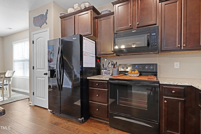 kitchen with dark wood-type flooring, baseboards, dark brown cabinets, light stone countertops, and black appliances