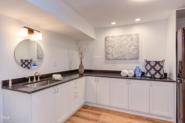 kitchen featuring dark stone countertops, a sink, light wood-style flooring, and white cabinetry