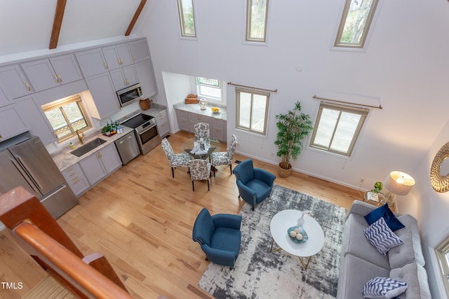 living area with high vaulted ceiling, beamed ceiling, light wood-type flooring, and baseboards