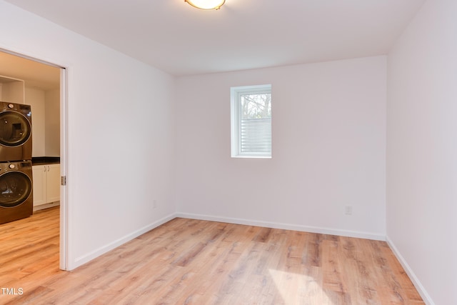 spare room featuring light wood-style flooring, stacked washer and clothes dryer, and baseboards