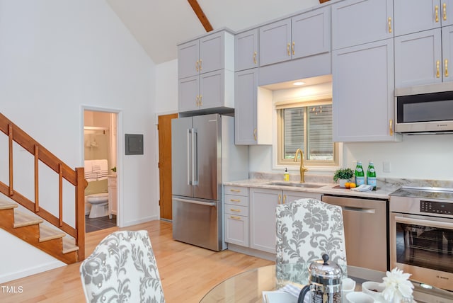 kitchen with high vaulted ceiling, a sink, light wood-style floors, appliances with stainless steel finishes, and light stone countertops