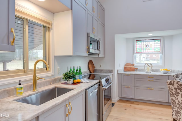 kitchen with stainless steel appliances, light wood finished floors, a sink, and light stone countertops