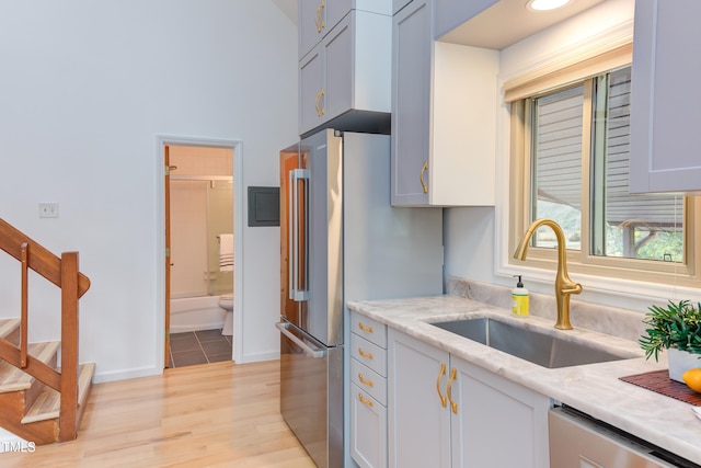 kitchen featuring light stone counters, stainless steel appliances, a sink, baseboards, and light wood-style floors