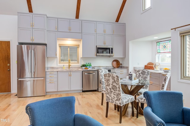 kitchen with beamed ceiling, light countertops, stainless steel appliances, light wood-type flooring, and a sink