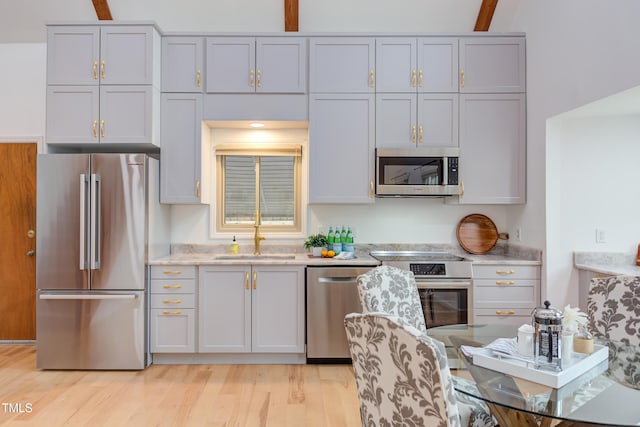 kitchen with appliances with stainless steel finishes, a sink, light stone countertops, light wood-style floors, and beam ceiling