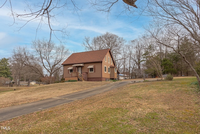 view of front facade featuring driveway, a shingled roof, and a front lawn