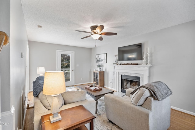 living area featuring baseboards, a ceiling fan, wood finished floors, a textured ceiling, and a high end fireplace