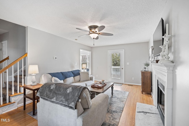 living room with a fireplace with flush hearth, ceiling fan, light wood-type flooring, baseboards, and stairs