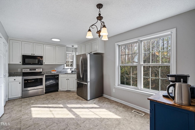 kitchen featuring baseboards, visible vents, white cabinets, decorative light fixtures, and black appliances