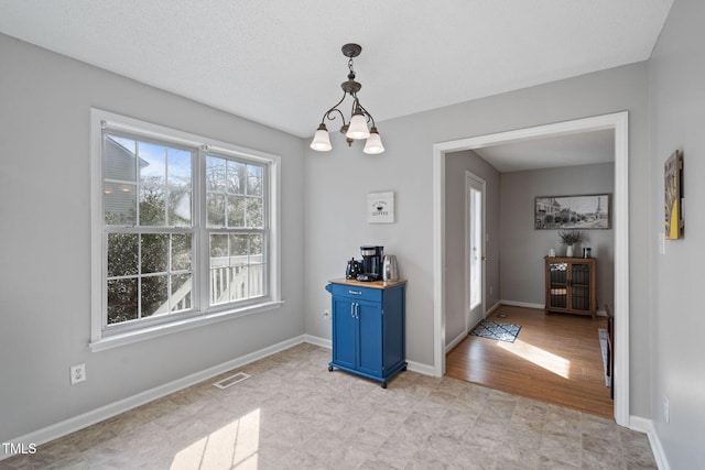 unfurnished dining area with visible vents, a notable chandelier, a textured ceiling, and baseboards