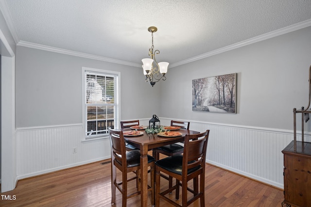 dining room with a textured ceiling, wainscoting, wood finished floors, and a chandelier