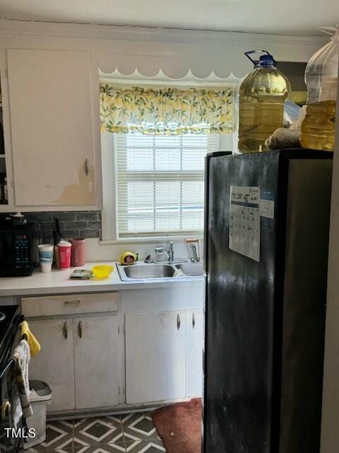 kitchen with a sink, white cabinets, light countertops, backsplash, and freestanding refrigerator