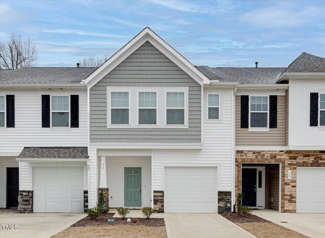 view of property featuring driveway, stone siding, and an attached garage