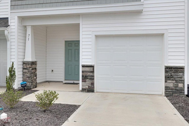 view of exterior entry with a garage, stone siding, and concrete driveway