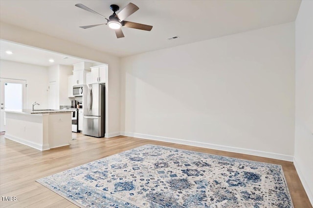 interior space featuring appliances with stainless steel finishes, light wood-style floors, white cabinetry, an island with sink, and baseboards