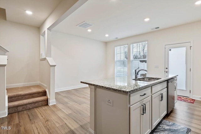 kitchen featuring a sink, visible vents, light wood-type flooring, light stone countertops, and dishwasher