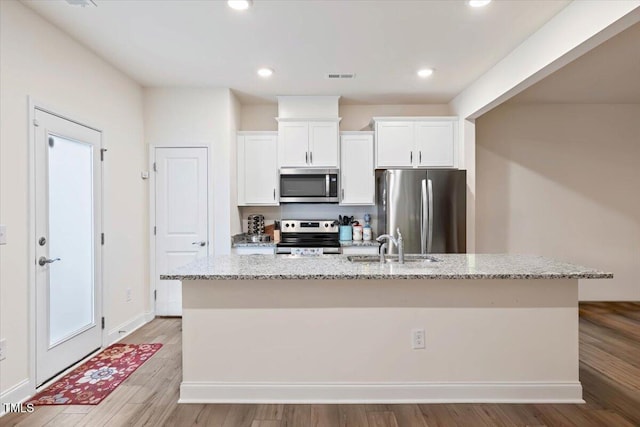 kitchen featuring light stone counters, visible vents, appliances with stainless steel finishes, white cabinets, and an island with sink