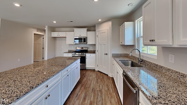 kitchen featuring stone counters, appliances with stainless steel finishes, white cabinets, and a sink