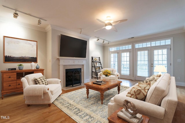 living area with ornamental molding, light wood-type flooring, a fireplace with flush hearth, and a ceiling fan