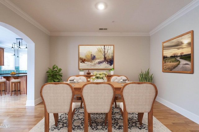 dining area with arched walkways, light wood-style floors, visible vents, and crown molding