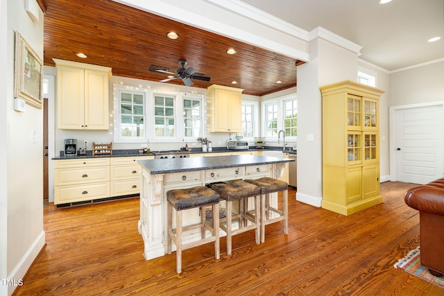 kitchen with ornamental molding, a center island, light wood finished floors, dark countertops, and a kitchen bar