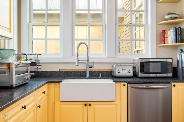 kitchen with open shelves, stainless steel appliances, dark countertops, light brown cabinets, and a sink