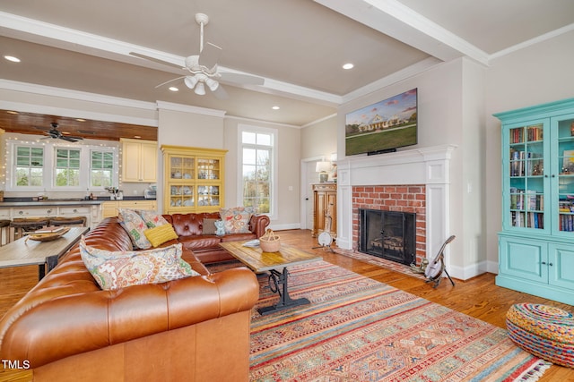 living area with a ceiling fan, a brick fireplace, light wood-style flooring, and crown molding