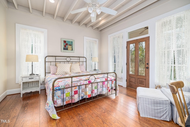 bedroom with beam ceiling, baseboards, and wood finished floors