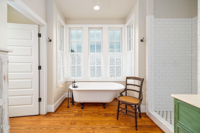 interior space with a freestanding tub, recessed lighting, wood finished floors, vanity, and baseboards