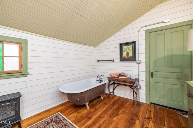 bathroom featuring wood finished floors, vaulted ceiling, a soaking tub, heating unit, and a wood stove