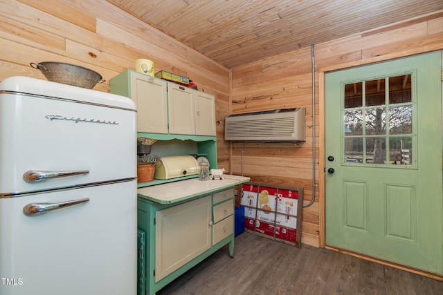 kitchen with dark wood-type flooring, freestanding refrigerator, light countertops, and wooden walls