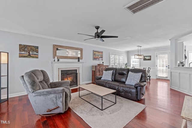 living room featuring crown molding, visible vents, dark wood-type flooring, a warm lit fireplace, and baseboards