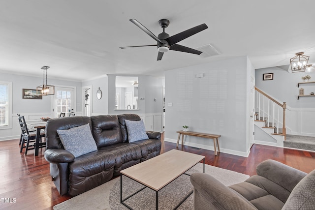 living area with stairs, ceiling fan with notable chandelier, wood finished floors, and crown molding