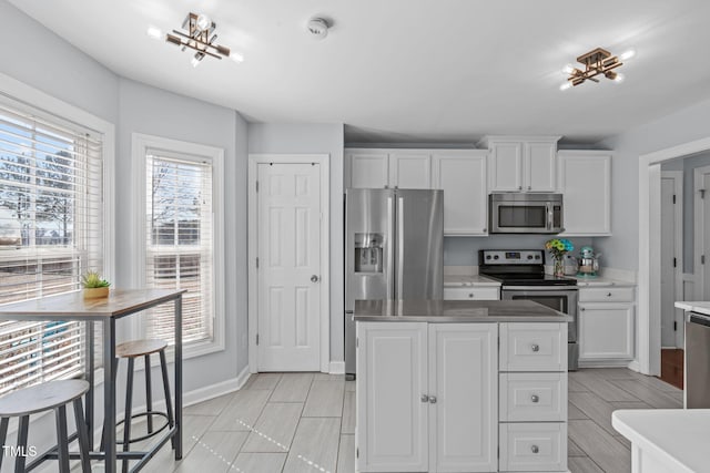 kitchen with a center island, stainless steel appliances, light countertops, white cabinets, and baseboards