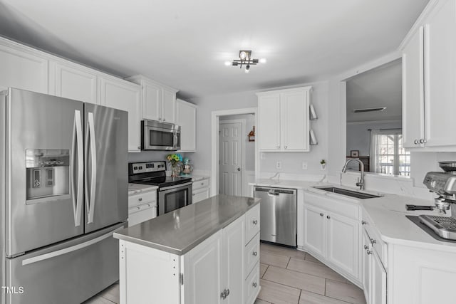 kitchen with a kitchen island, appliances with stainless steel finishes, light stone countertops, white cabinetry, and a sink