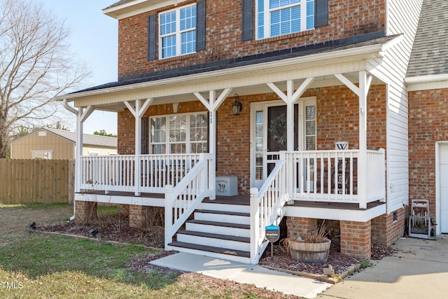 property entrance featuring roof with shingles, fence, a porch, and brick siding