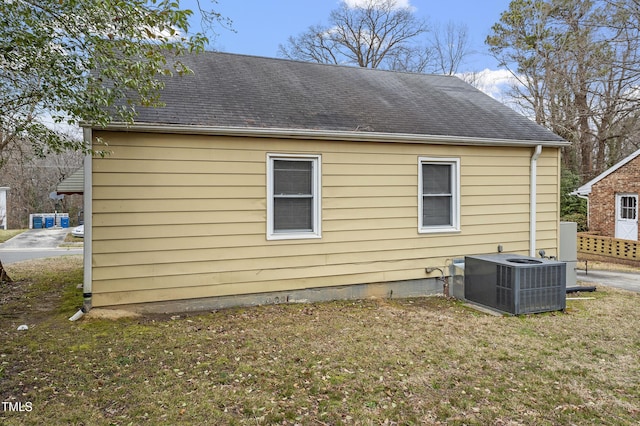 view of side of property featuring a yard, a shingled roof, and central AC