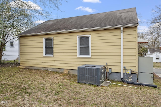 rear view of house with a yard, roof with shingles, and central AC unit