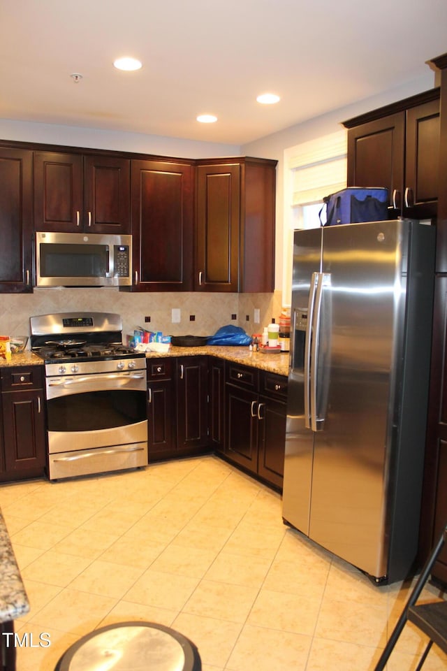 kitchen featuring dark brown cabinets, appliances with stainless steel finishes, backsplash, and light stone counters