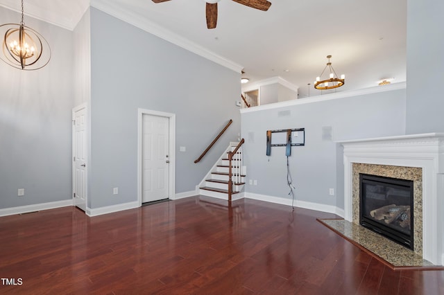 unfurnished living room with stairway, wood finished floors, a fireplace, crown molding, and ceiling fan with notable chandelier